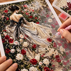 A hand placing drills on a diamond painting of a woman in an ivory gown in a red and white rose garden