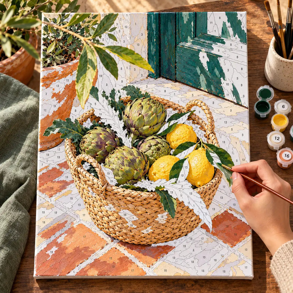 `04-artichokes-lemons-market-basket-painting-process.webp` — Painting process scene for the Artichokes Lemons Market Basket kit, with the complete numbered canvas and painting tools.
