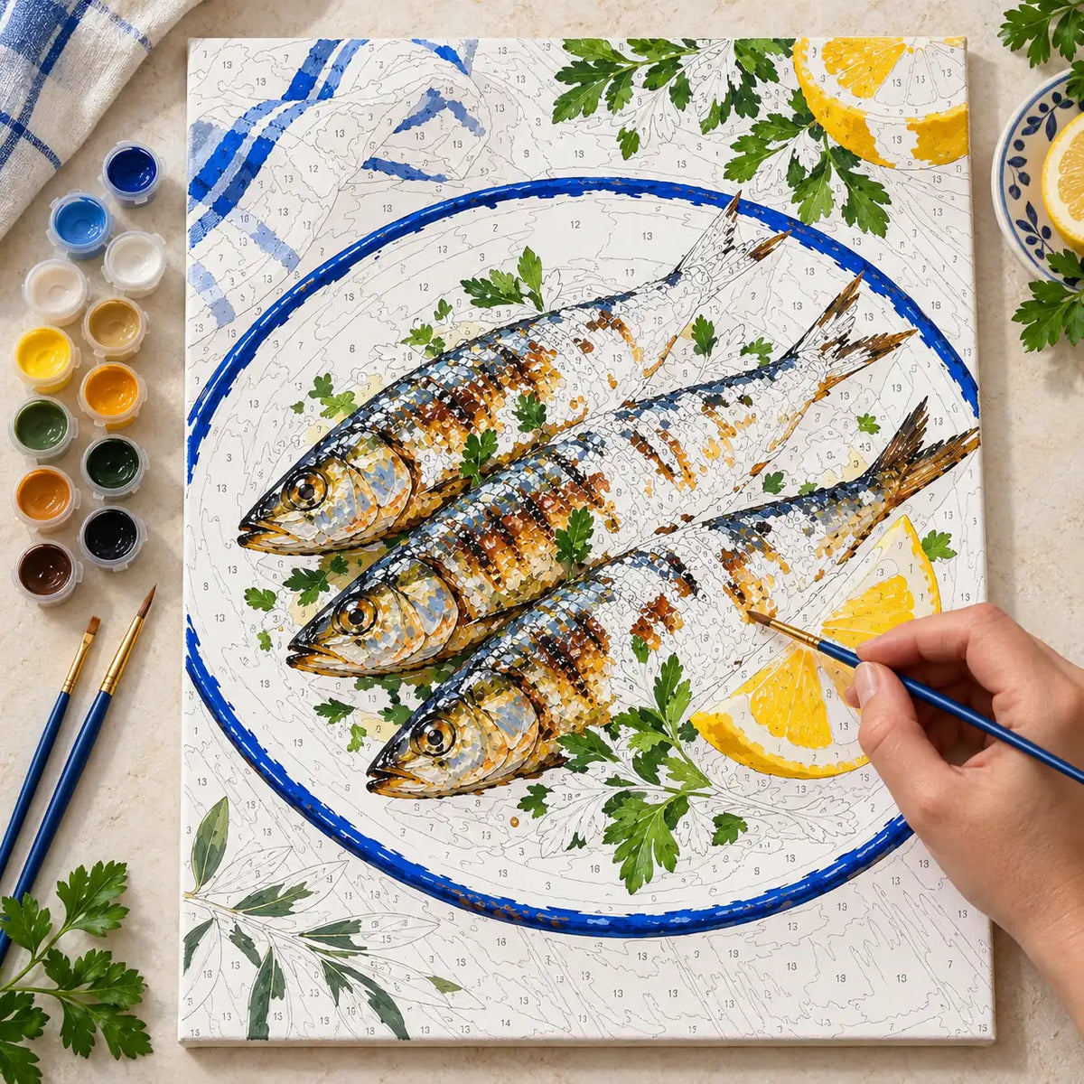 Painting process scene for the Sardines Lemon Enamel Plate kit, with the complete numbered canvas and painting tools.