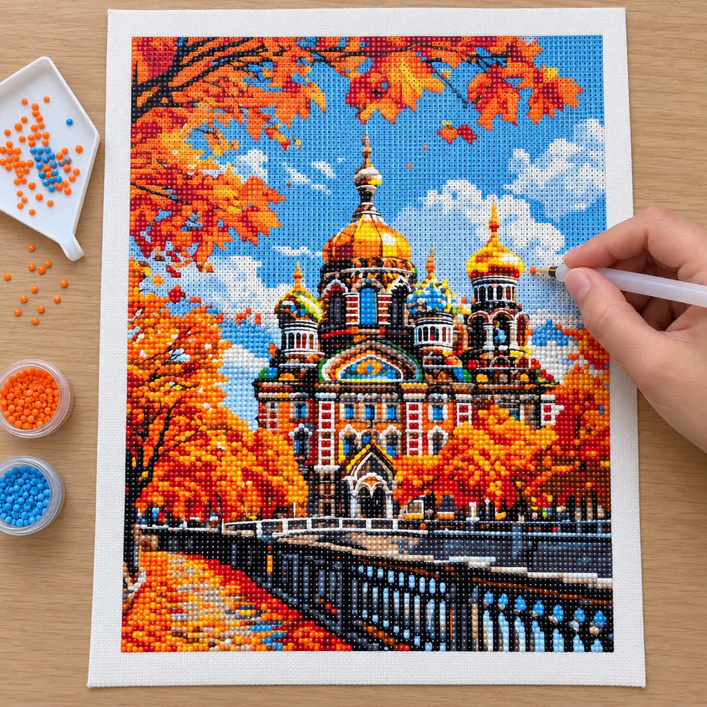 Hands applying drills to a canvas showing an ornate cathedral with golden domes among orange autumn leaves.