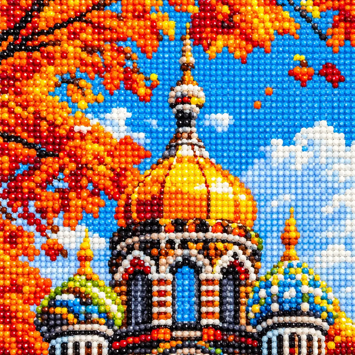 Close-up of diamond drills on artwork showing an ornate cathedral with golden domes among orange autumn leaves.