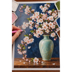 Pale pink cherry blossoms arranged in a celadon vase against a deep blue background: diamond painting in progress with a pen