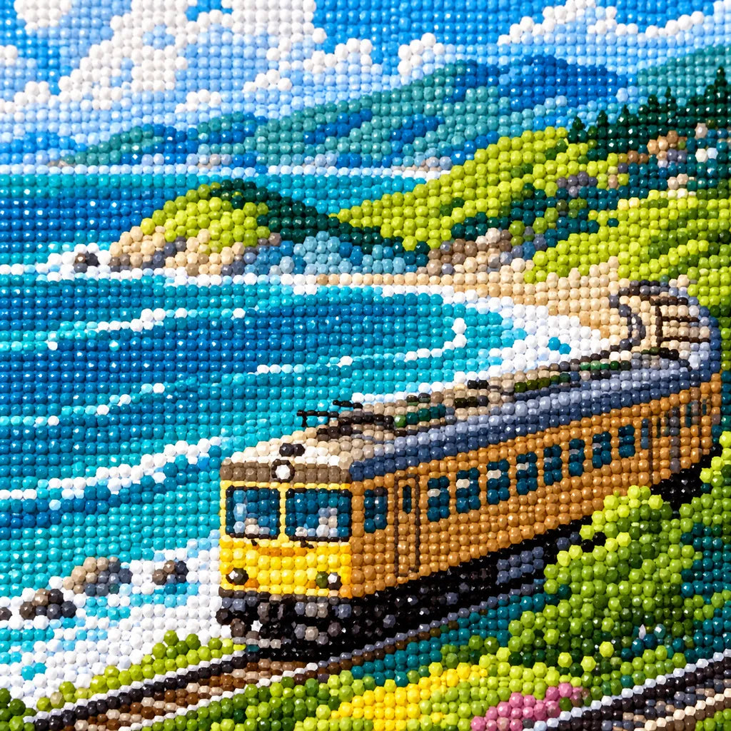 Close-up detail of drill texture across a yellow train winding beside turquoise surf and green coastal cliffs.