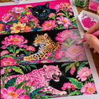 Hands applying drills to a canvas with three big cats among vivid tropical flowers and foliage.
