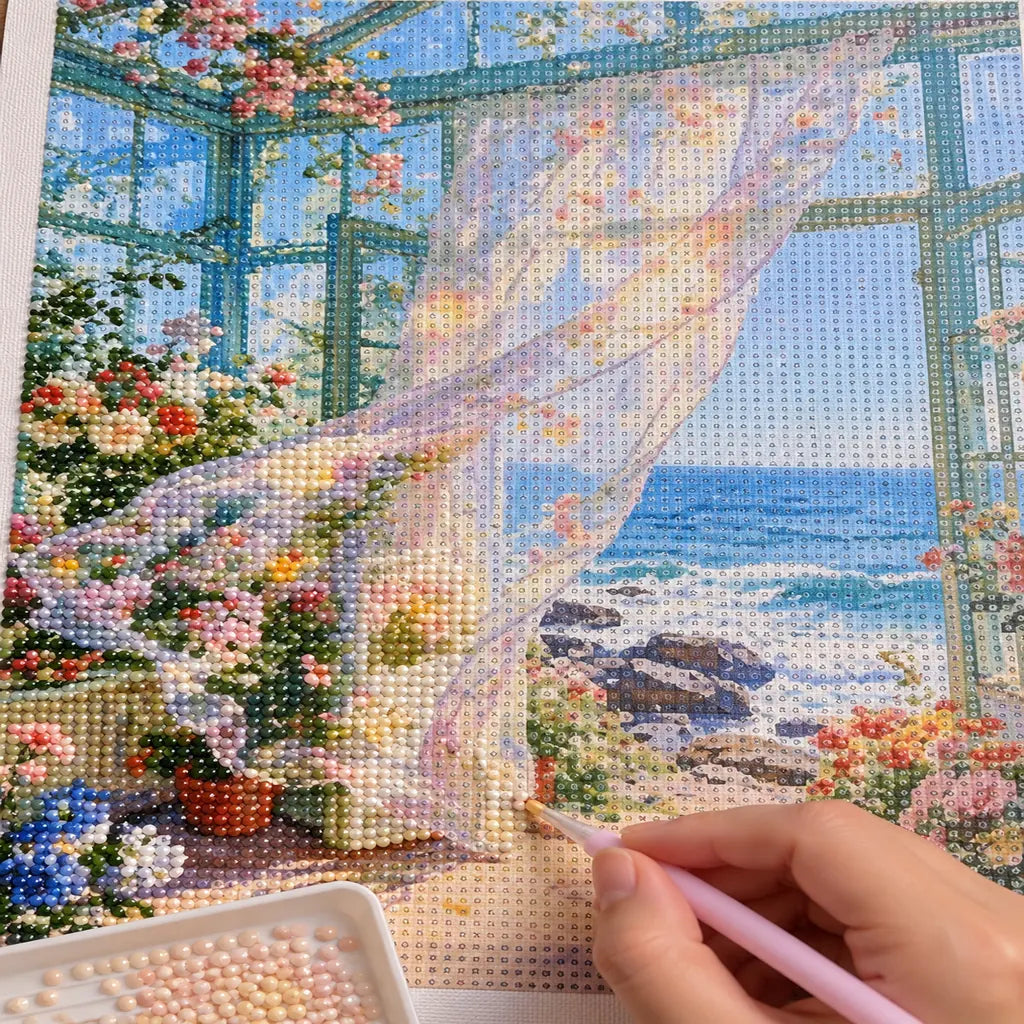 a hand placing diamonds on a rocky ocean conservatory with flowing curtains — process image, diamond painting kit