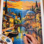 Diamond painting process for Golden Hour by the Canal, showing drills being placed over boats and old-town buildings reflected in a golden canal at sunset.