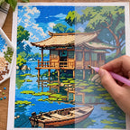 Diamond painting process for Lakeside Serenity, showing drills being placed over a wooden cabin and rowboat beside a calm tree-lined lake.