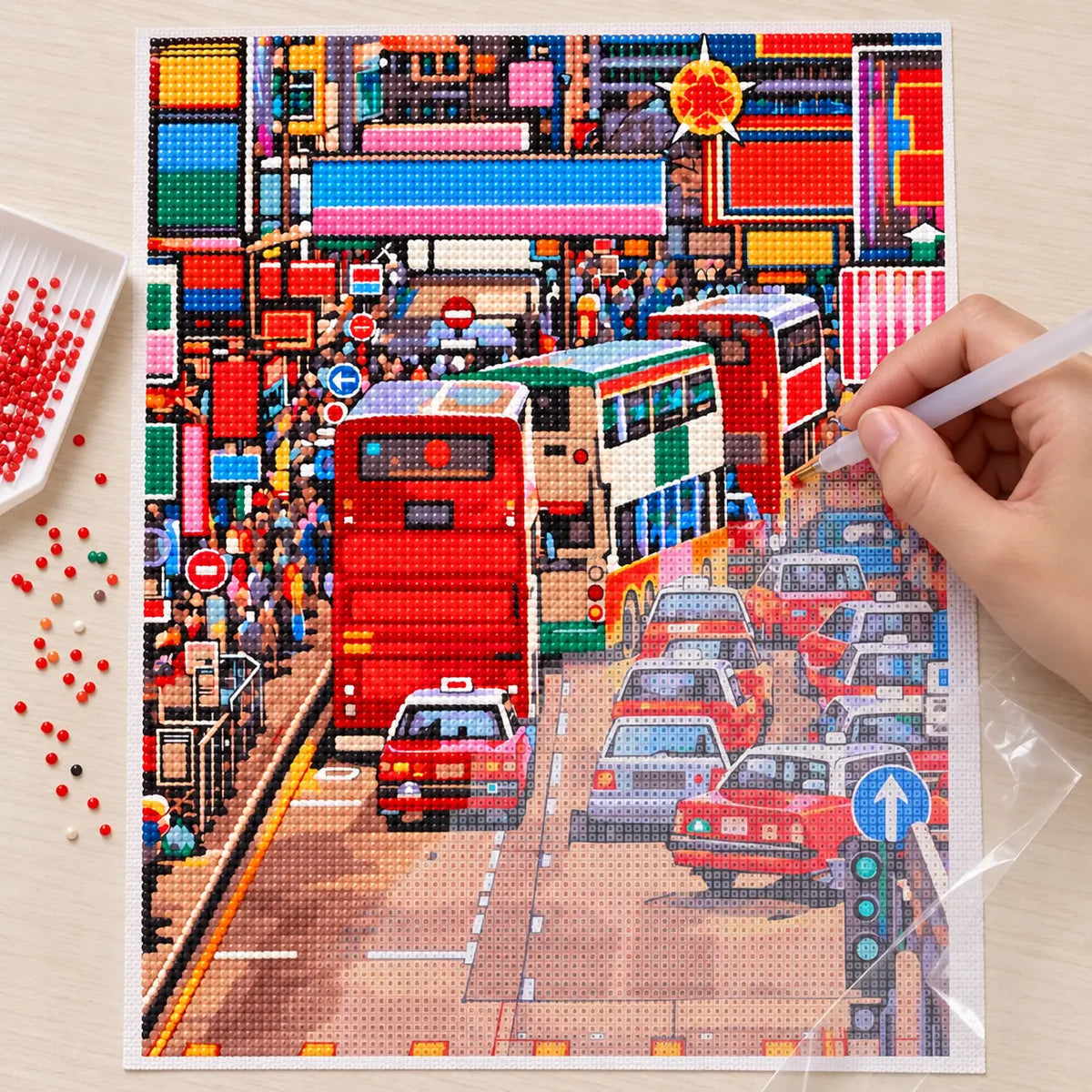 Hands applying drills to a canvas showing a busy Kowloon street with red double-decker buses and dense city traffic.