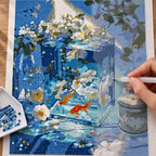 Diamond painting process for Serene Blue Aquarium Diamond Painting Kit, with hands applying drills over a orange goldfish swimming among white blossoms inside a blue glass aquarium.