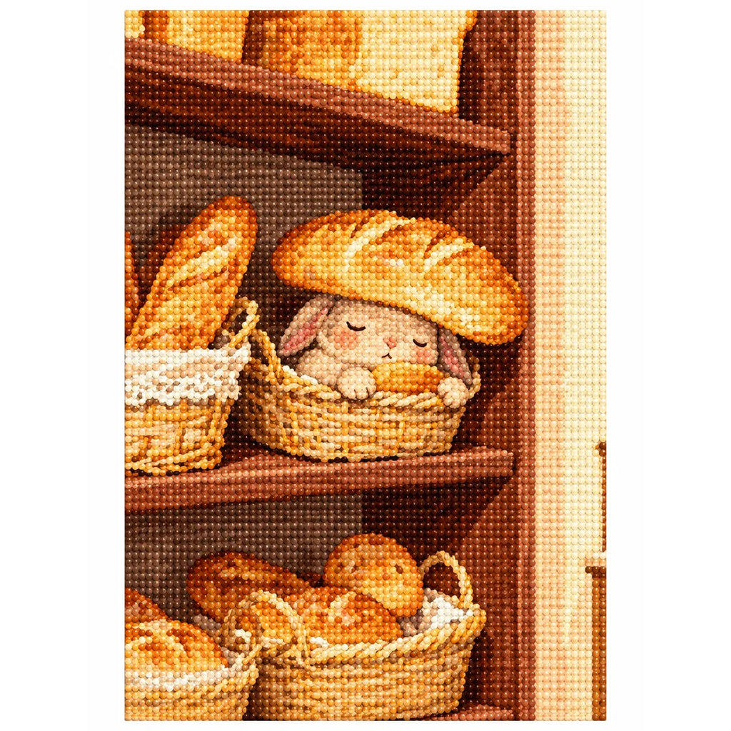 White-background diamondized artwork of a sleepy bunny tucked into a woven bread basket beneath a loaf