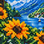 Close-up of drill texture and color in golden sunflowers beside a blue mountain lake and distant village.