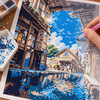 Diamond painting process for Sunlit Village Passage, with drills being placed over a sunlit stone passage opening onto blue water between old village buildings.