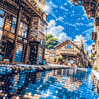 Close-up of diamond drill texture across a sunlit stone passage opening onto blue water between old village buildings.