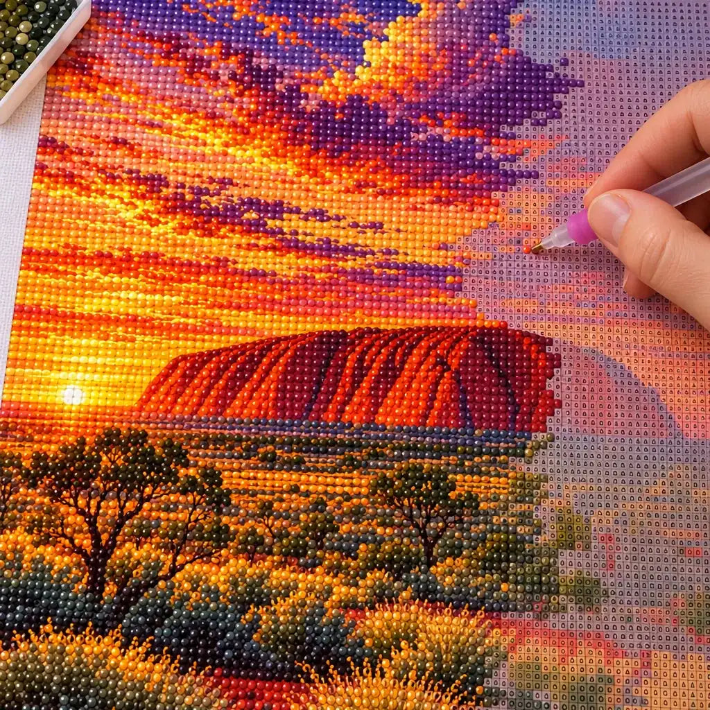 Hands placing diamond drills on the Uluru Sunset design.